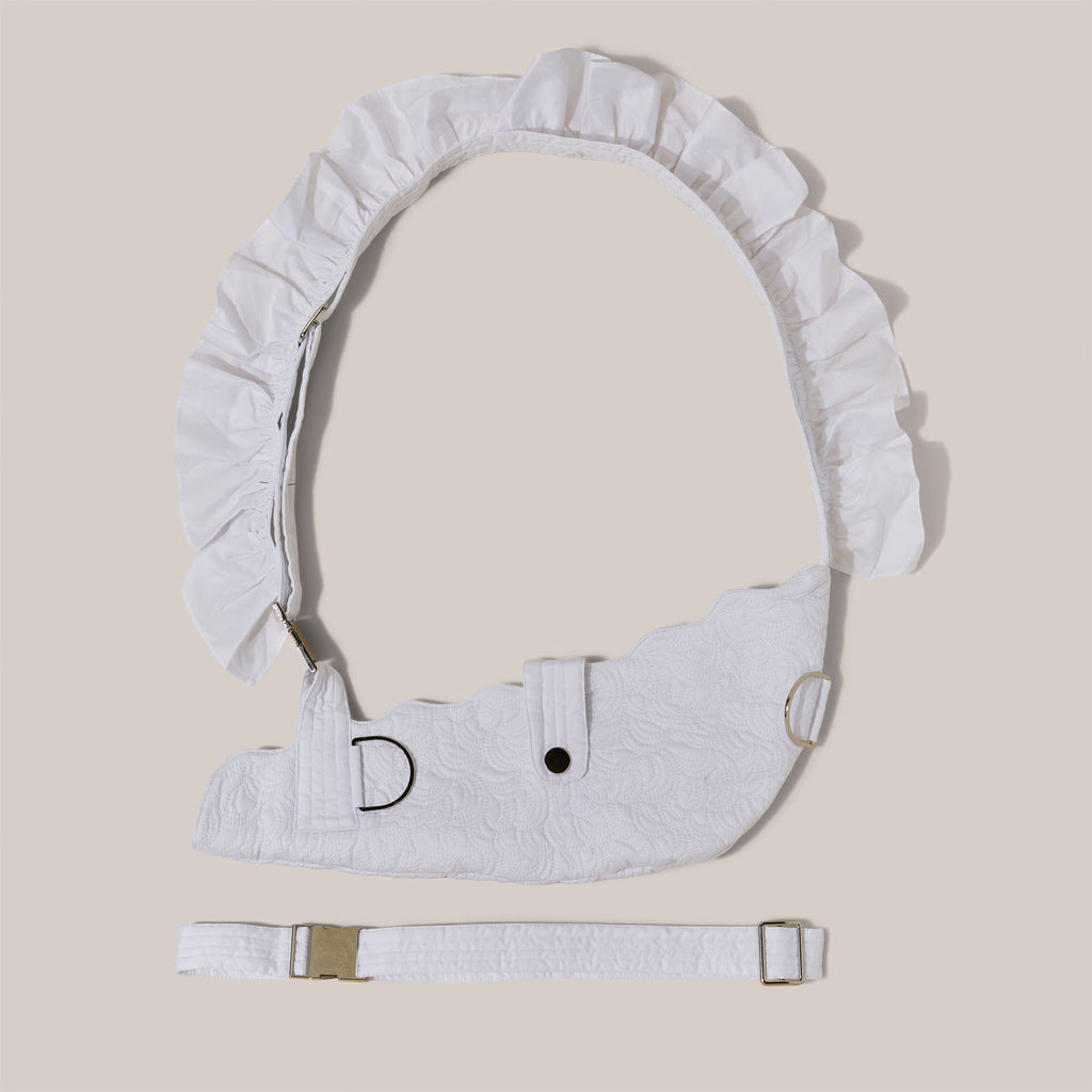 White embroidered arm sling with detachable frill on shoulder strap against a studio ackground.