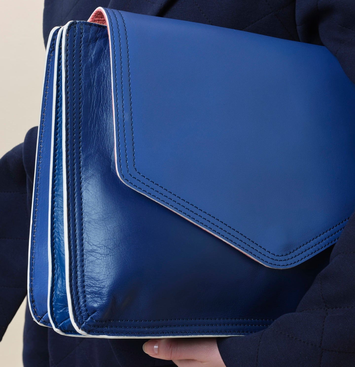 Large blue leather document folio for notes and papers associated with patient journey such as consultant notes, hospital appointments and health insurance documents. This folio is held by a woman in a navy blue jacket designed for recovery and or chemotherapy.