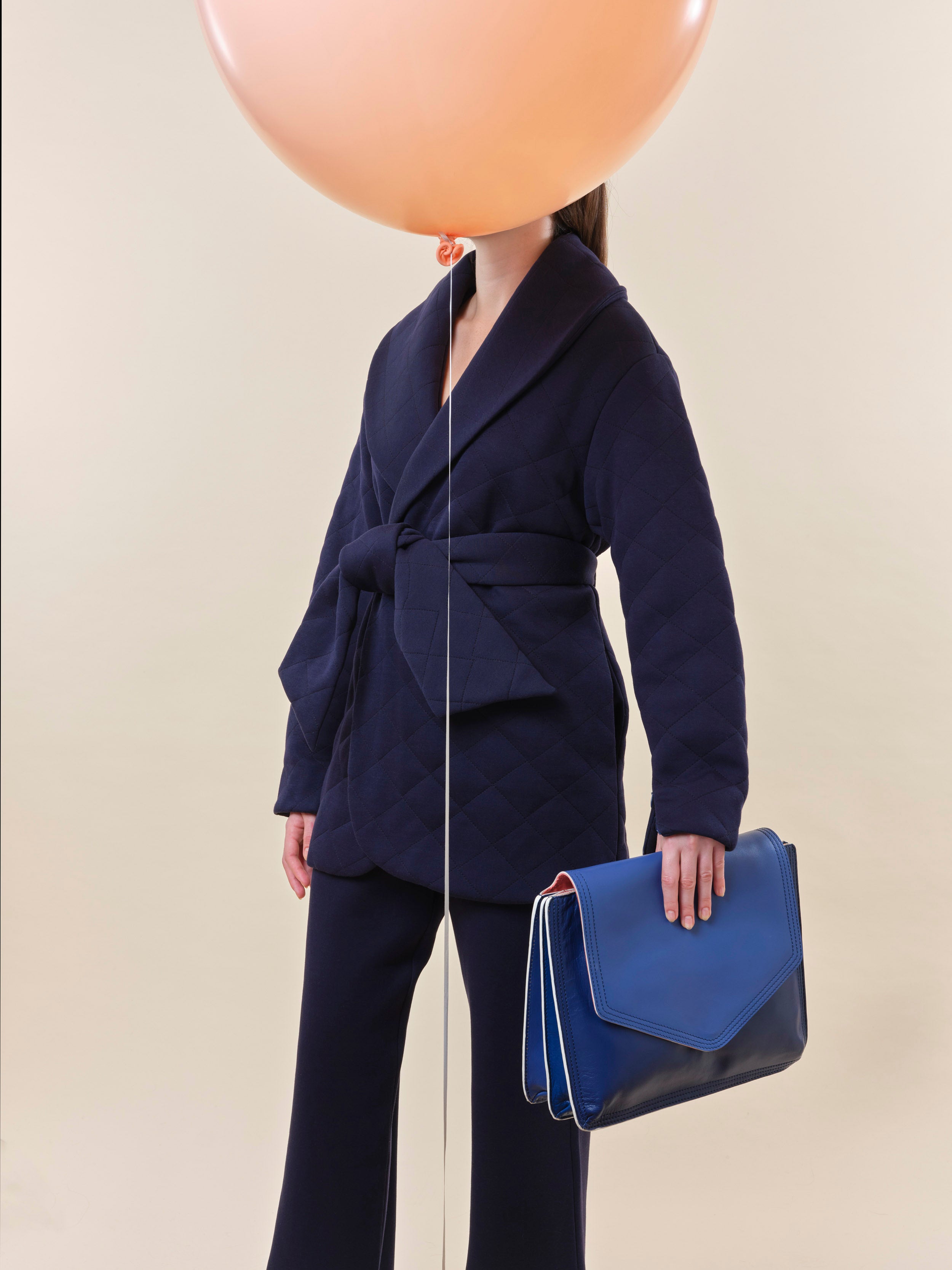 Large blue leather document folio for notes and papers associated with patient journey such as consultant notes, hospital appointments and health insurance documents. This folio is held by a woman in a navy blue jacket and trousers designed for recovery and or chemotherapy.