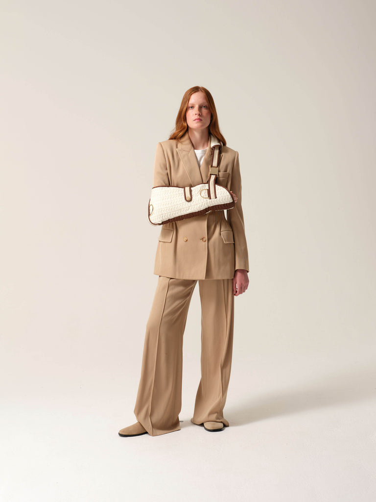 Woman in a camel coloured suit wearing a cashmere knit shearling lined arm sling against a studio background.