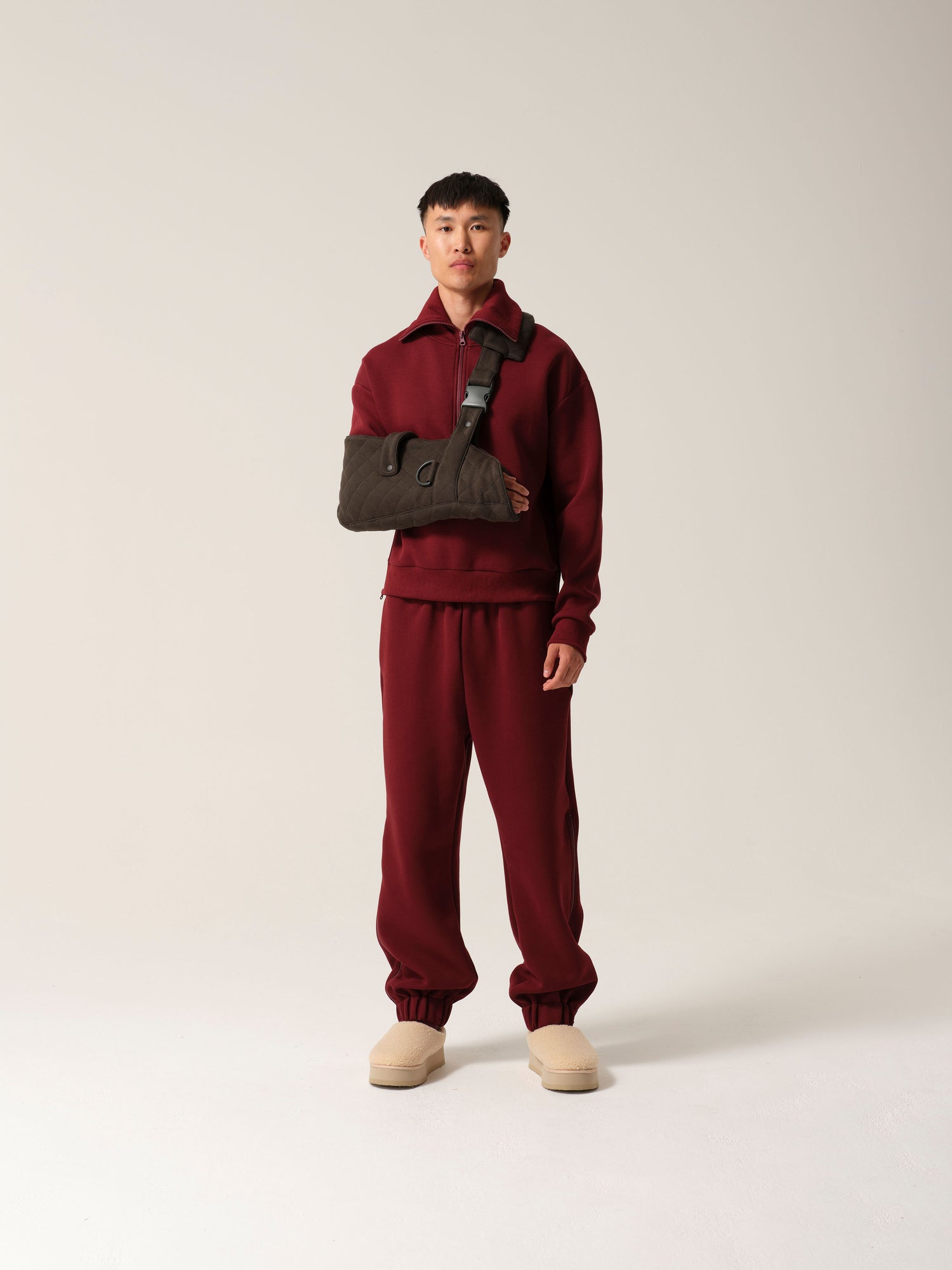 A man wearing breathable cotton forest green jersey arm sling with a wide shoulder strap and  recycled plastic hardware over burgundy luxe tracksuit.