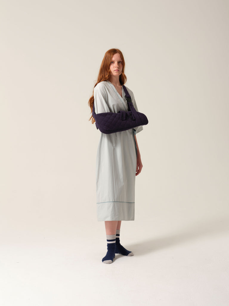 Woman in mint coloured patient gown weartng Navy jersey arm sling with a wide shoulder strap and recycled plastic hardware.