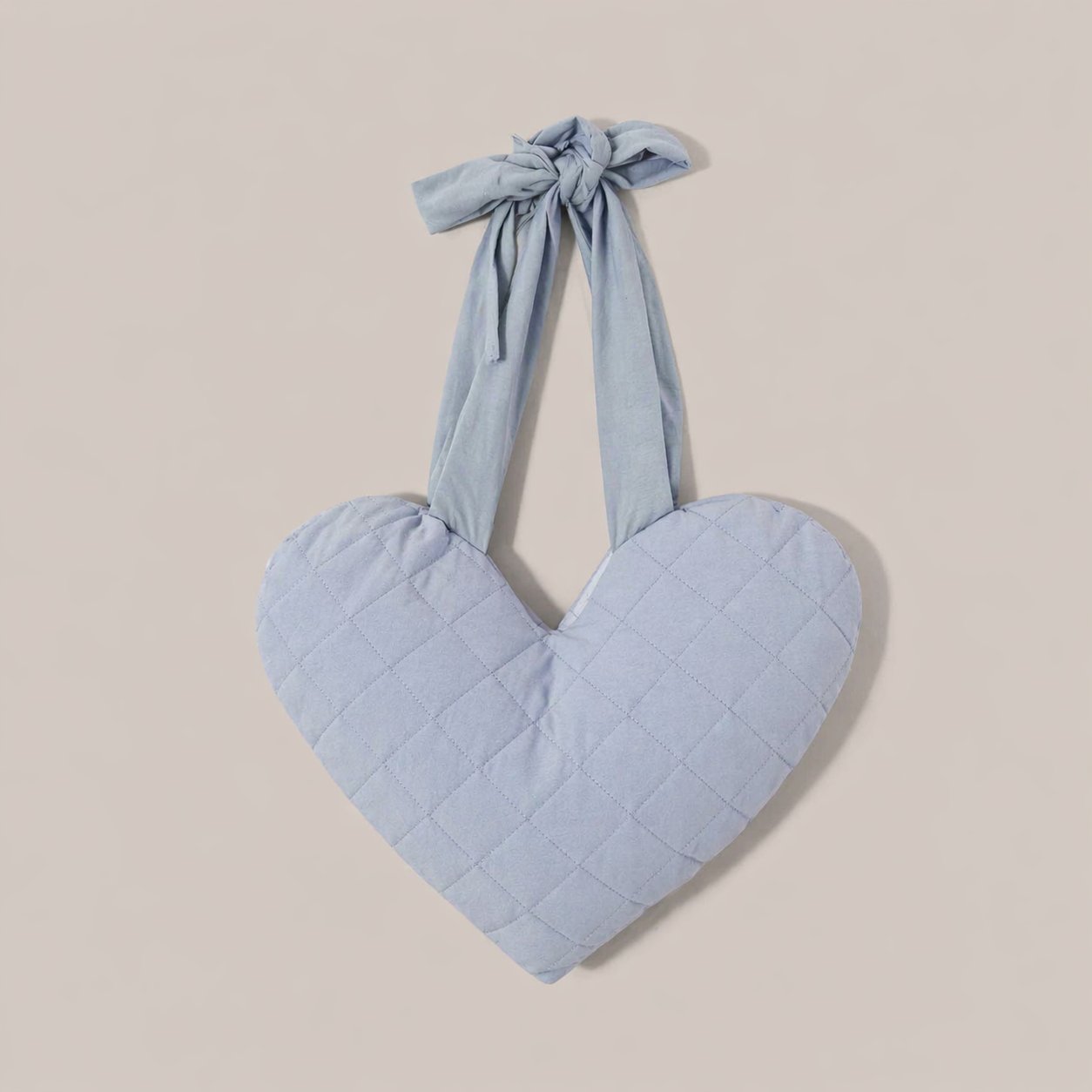 Heart-shaped blue mastectomy support pillow with bow on a beige background