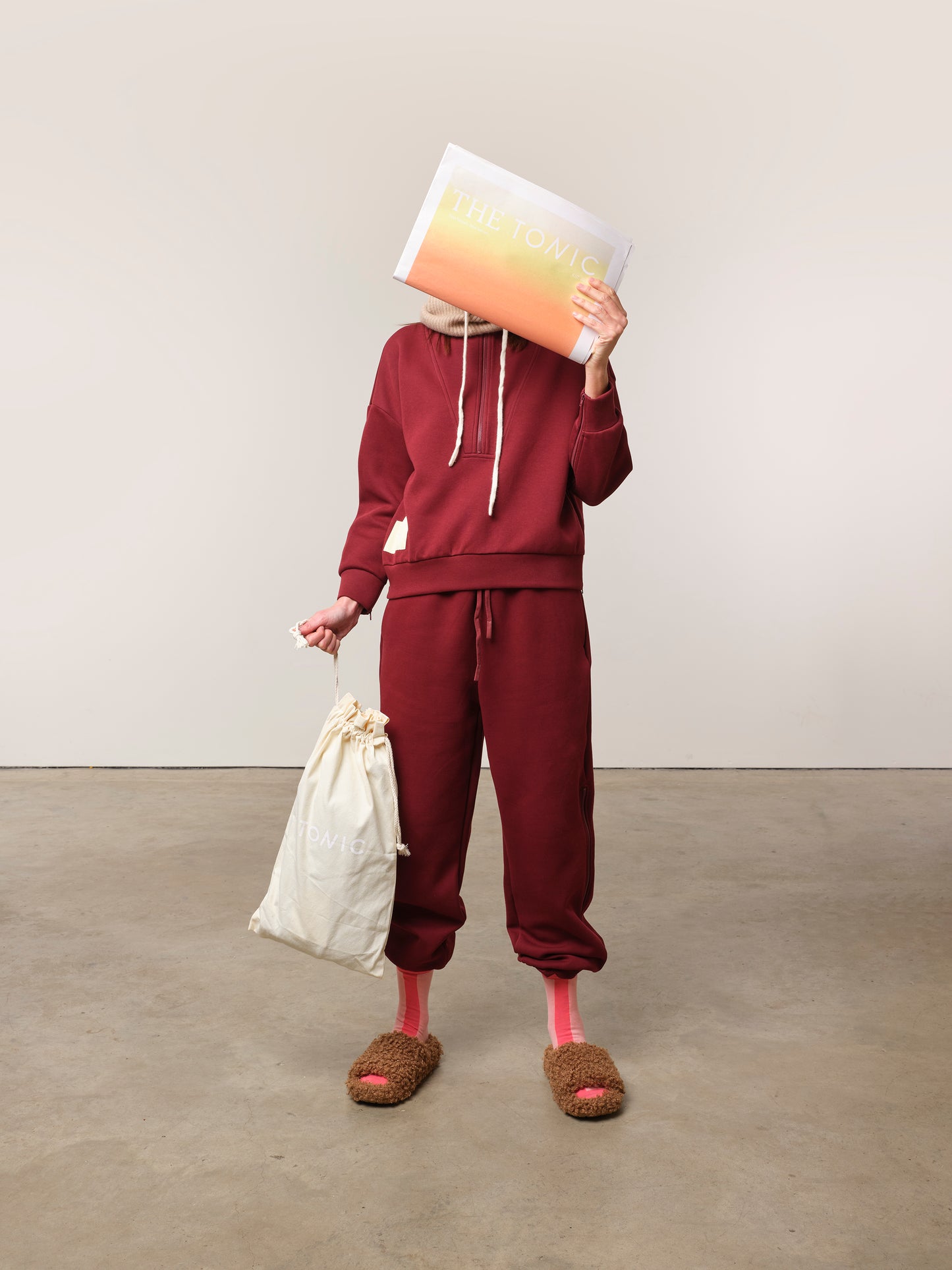 Image of model in TONIC burgundy chemotherapy tracksuit with newspaper covering her face.