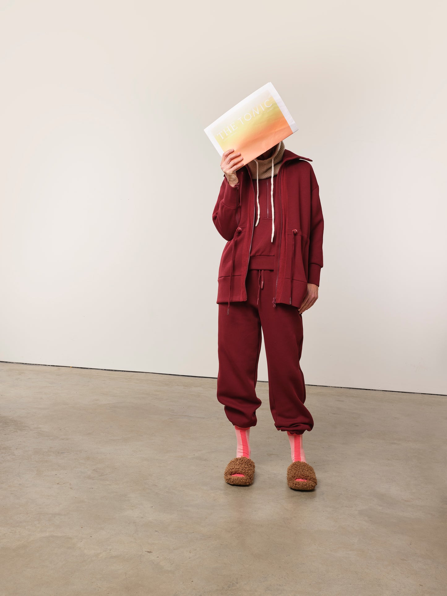 Image of model in TONIC burgundy chemotherapy tracksuit with newspaper covering her face.