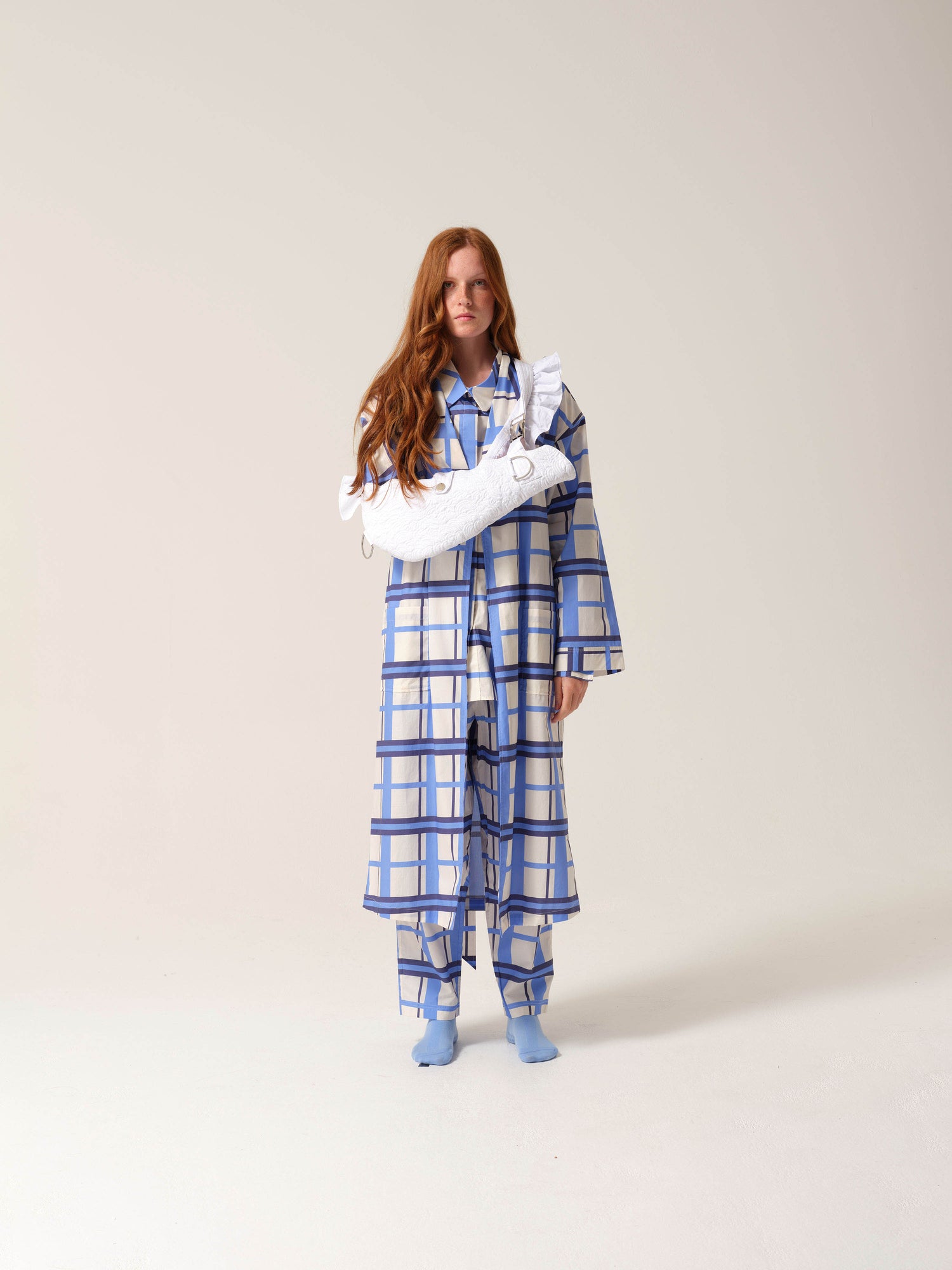 Woman wearing blue and white checkered pyjamas with a white embroidered arm sling against a studio ackground.