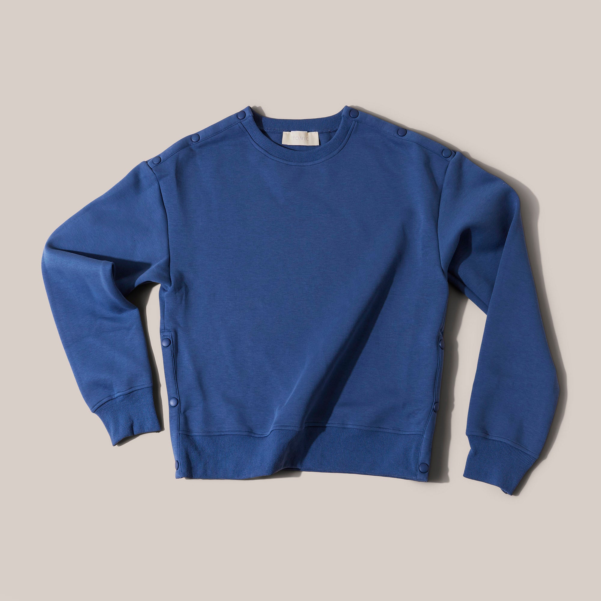 Front image product shot of TONIC Mens Hug Tracksuit sweatshirt top in ocean blue. Clinician-approved adaptive recovery tracksuit with popper access at the arms, neck, and legs for chemotherapy or feeding tubes. Made from breathable technical fabric that’s gentle on hypersensitive skin and ideal for post-surgery comfort.