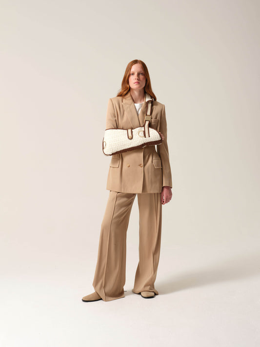 Woman in a camel coloured suit wearing a cashmere knit shearling lined arm sling against a studio background.