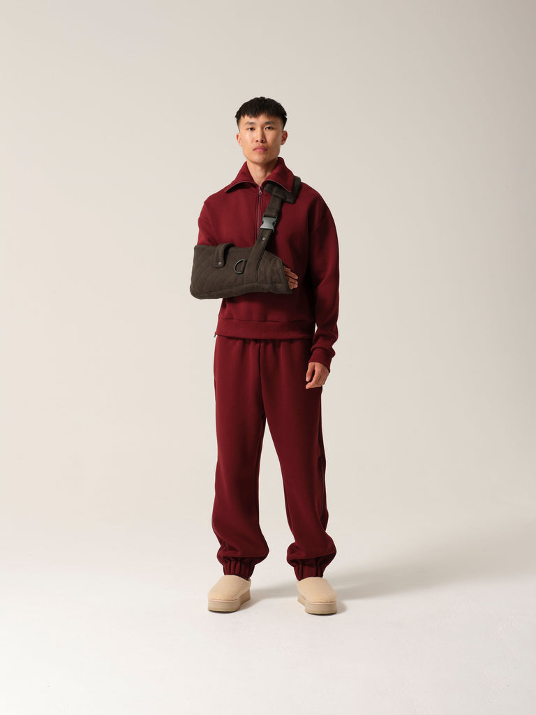 A man wearing breathable cotton forest green jersey arm sling with a wide shoulder strap and  recycled plastic hardware over burgundy luxe tracksuit.
