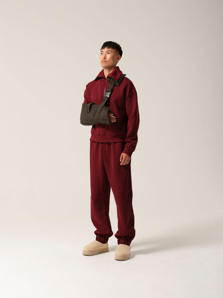A man wearing breathable cotton forest green jersey arm sling with a wide shoulder strap and  recycled plastic hardware over burgundy luxe tracksuit.