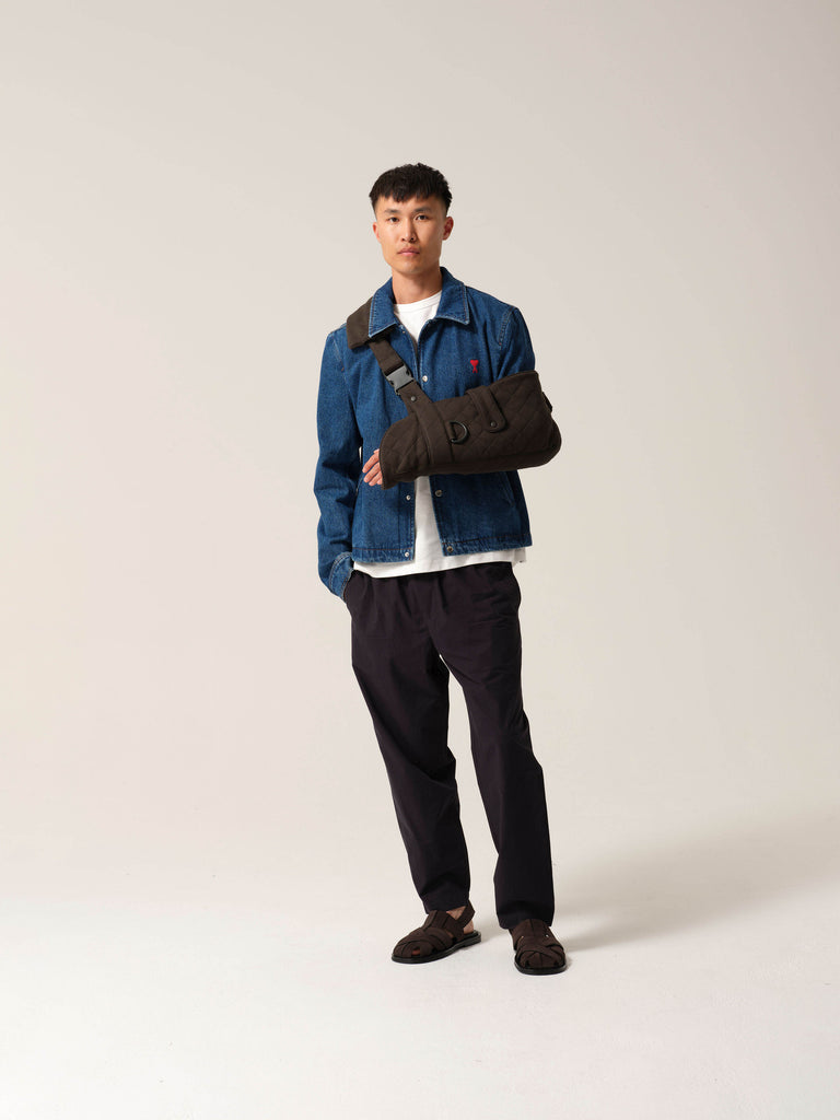 Man wearing forest green jersey arm sling with a wide shoulder strap and  recycled plastic hardware over denim work jacket.