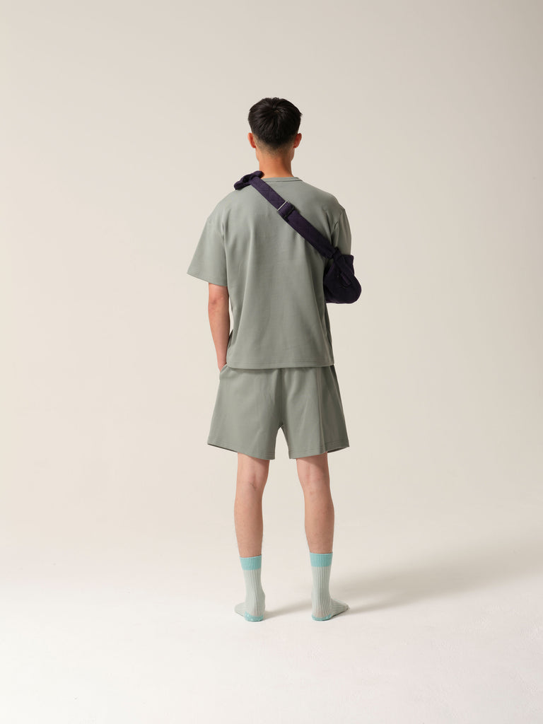 Backview of man wearing a mint green tshirt and shorts weartng Navy jersey arm sling with a wide shoulder strap and  recycled plastic hardware against a plain background.