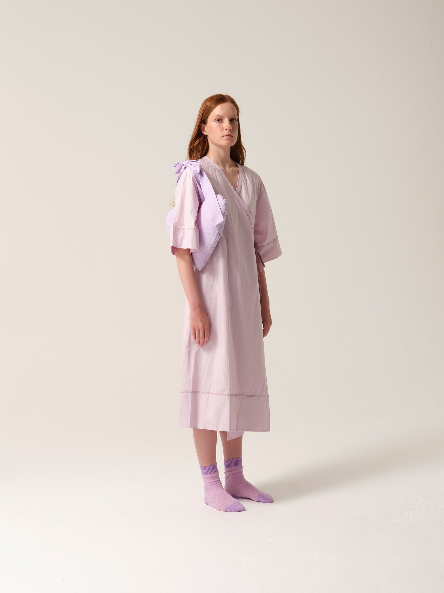 Woman wearing a lilac patient gown with lilac breast heart post mastectomy breast pilow on a white background