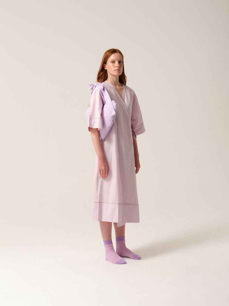 Woman wearing a lilac patient gown with lilac breast heart post mastectomy breast pilow on a white background