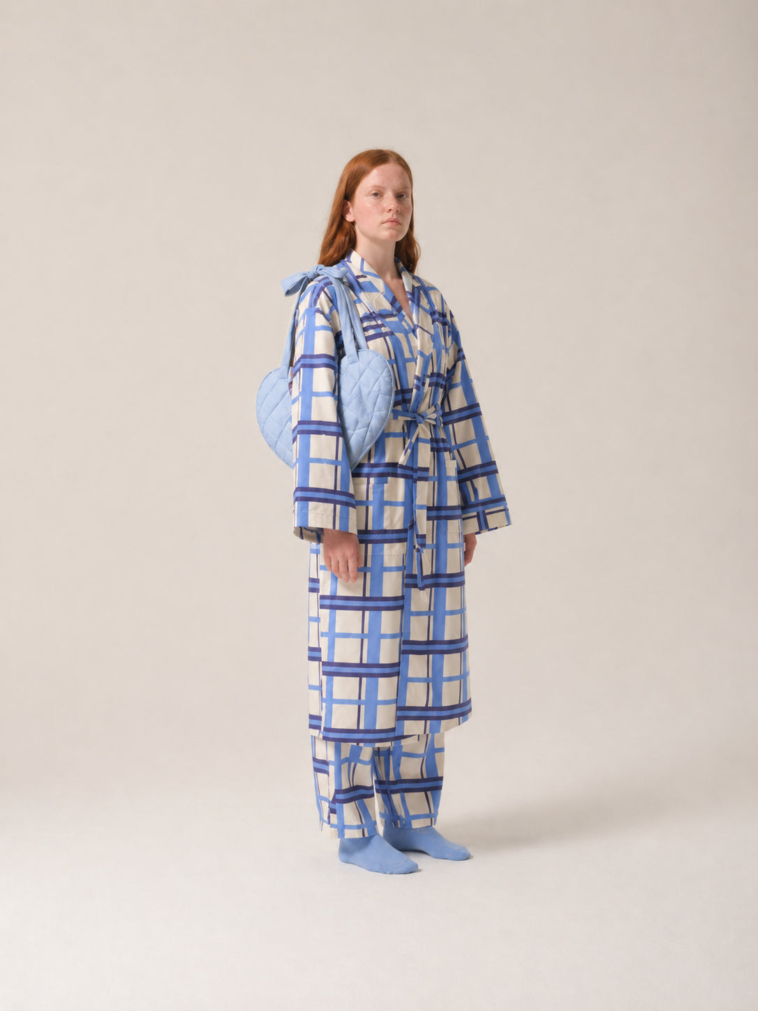Person wearing a blue and white checkered pyjamas with a light blue post mastecomy support pillow on a plain background