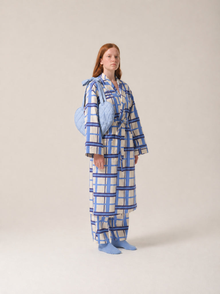 Person wearing a blue and white checkered pyjamas with a light blue post mastecomy support pillow on a plain background