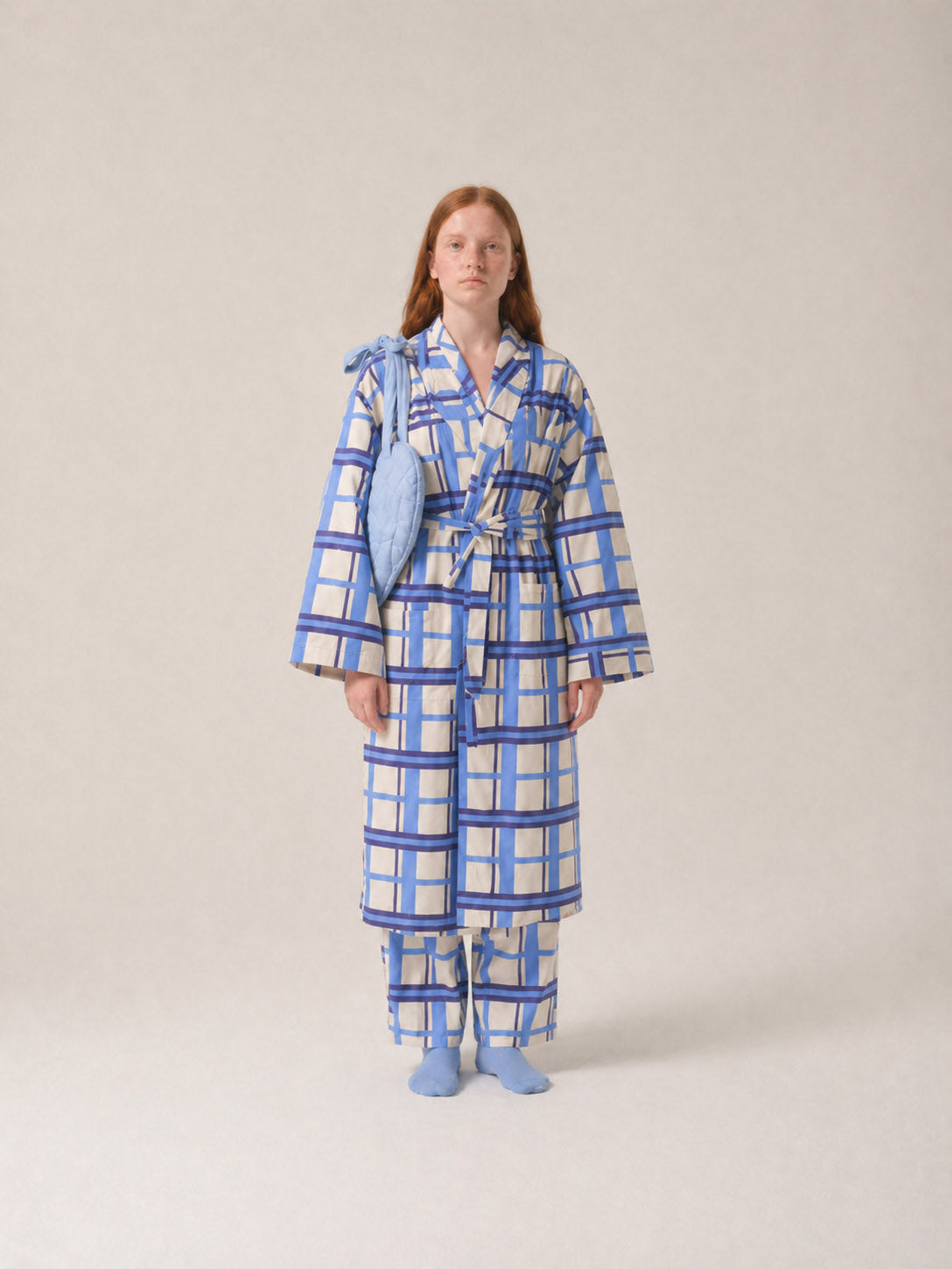 Person wearing a blue and white checkered robe and pyjamas with a light blue breast heart on a beige background