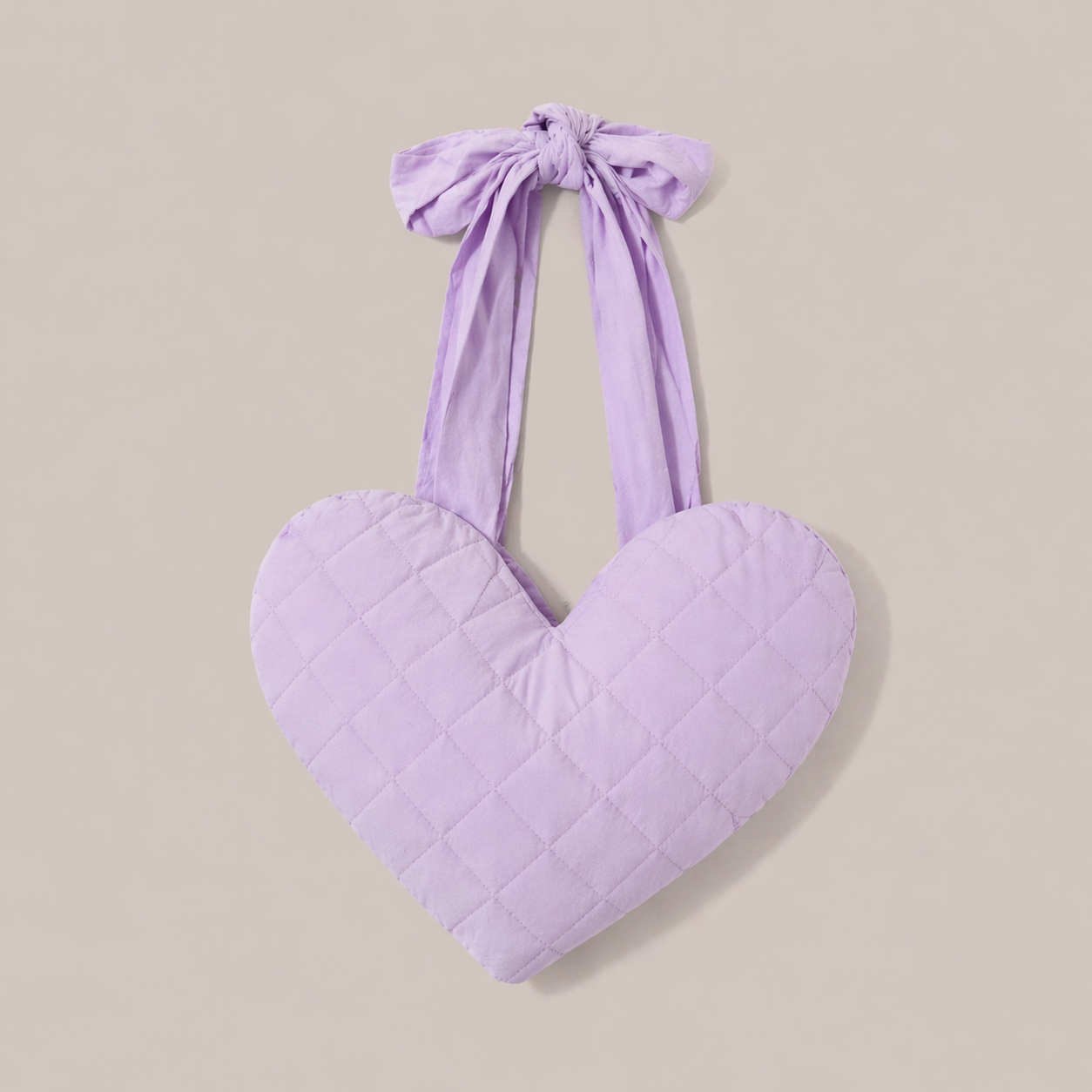 Heart-shaped lilac post mastectomy breast pillow with ribbon straps on a beige background