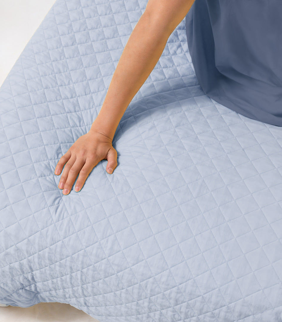 Person adjusting a light blue quilt on a bed