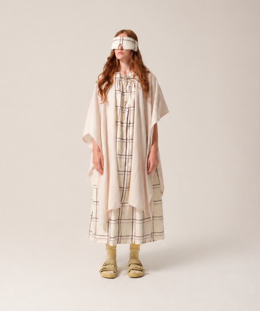 Woman Person wearing a checkered patient hospital gown and a white headband on a plain background and cashmere recuperation shawl from TONIC London patient wear