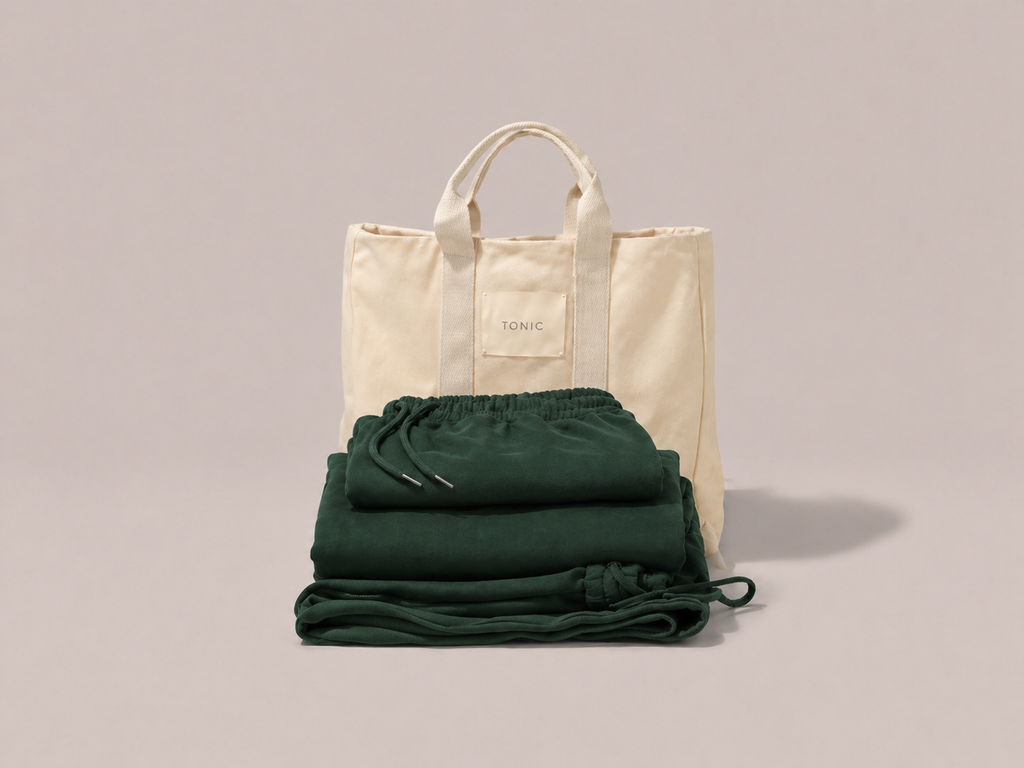 Hospital Bag in Beige tote bag size with green tracksuit folded in front on a light gray studio background