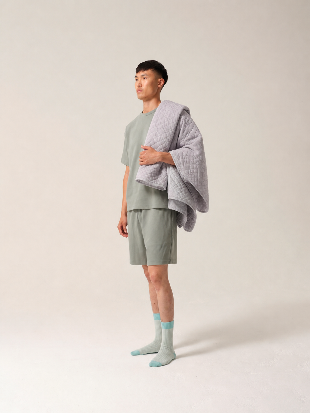 Man wearing a light green physio shorts set with a gray blanket draped over his shoulders against a plain background