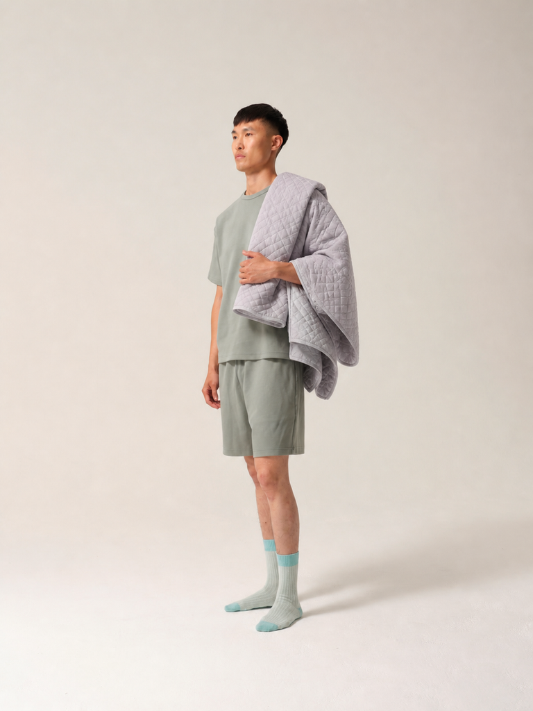 Man wearing a light green physio shorts set with a gray blanket draped over his shoulders against a plain background
